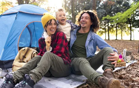 A couple and their young child laughing in front of their tent while camping.
