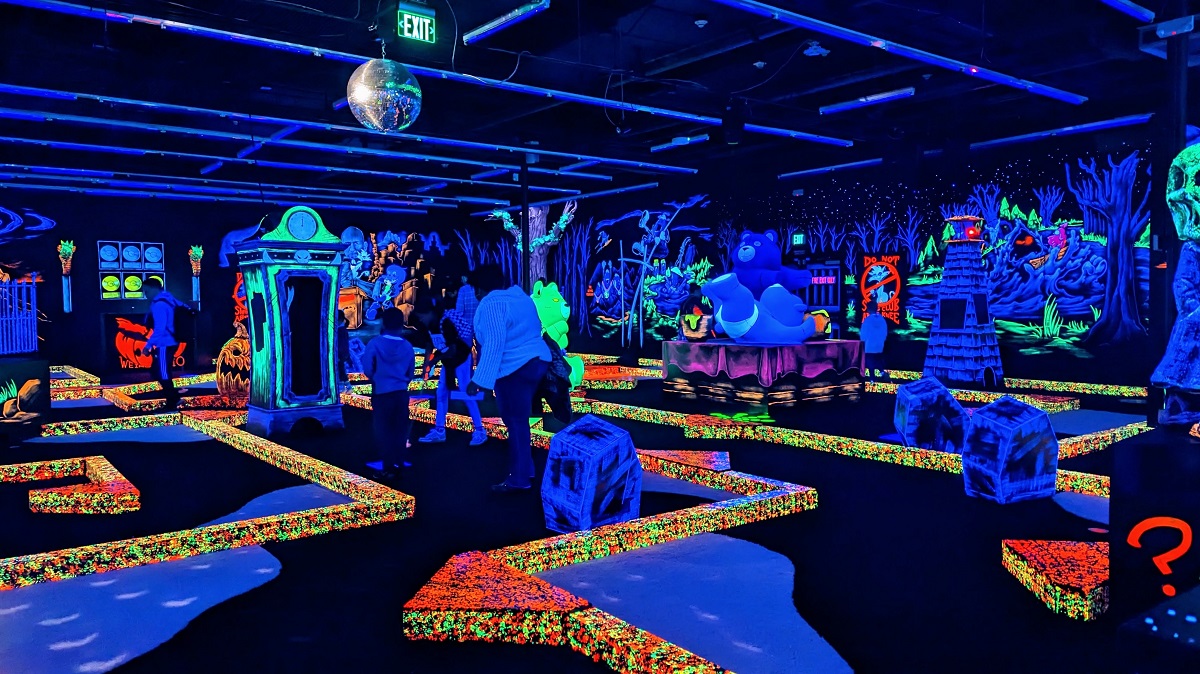 Kids and families play mini golf in a blacklight environment at Bellevue, Washington's new Monster Mini Golf family entertainment near Seattle
