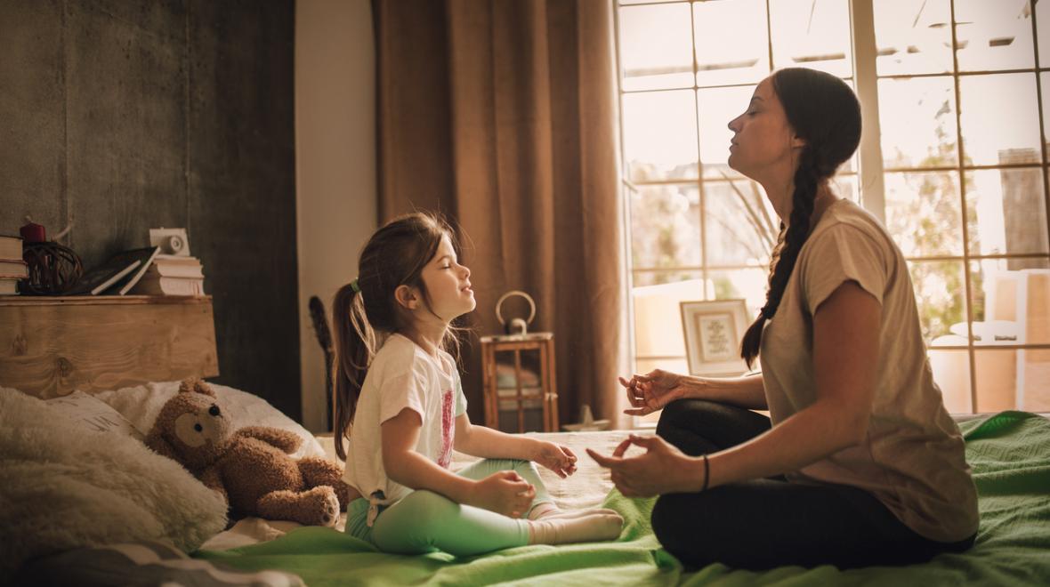 Mother and daughter practice meditation sitting on a bed