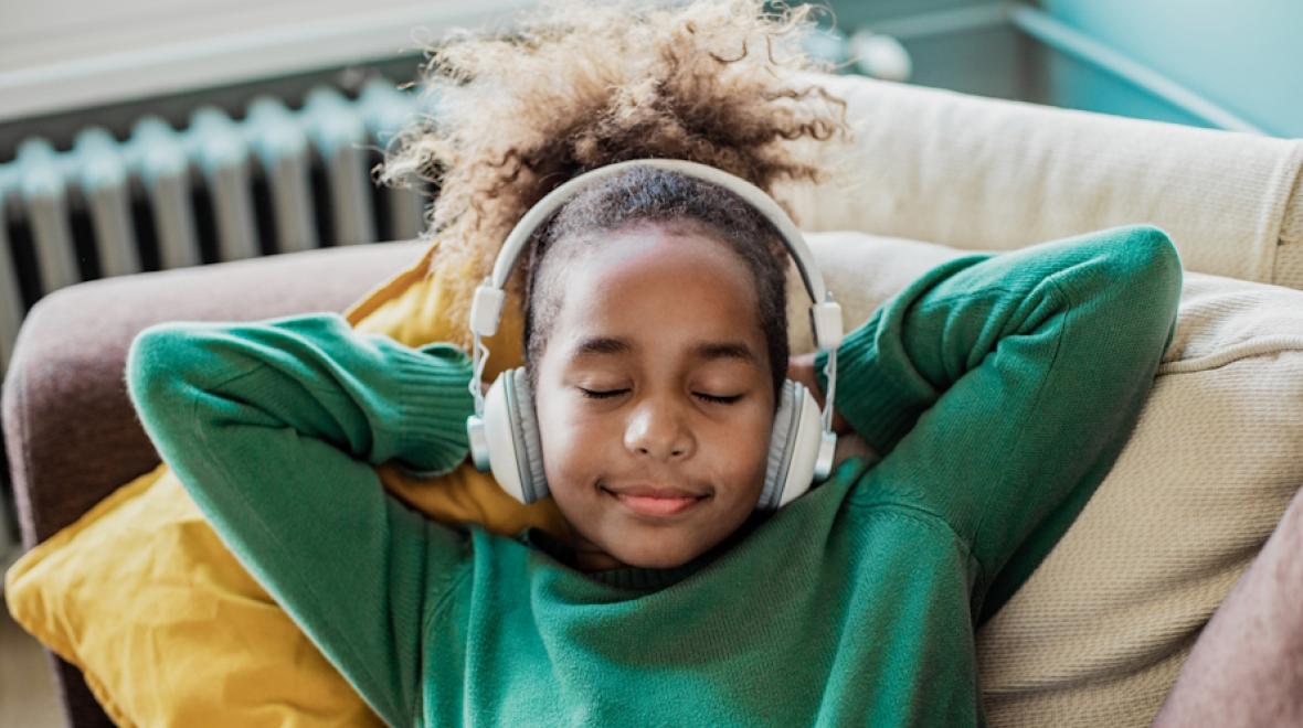 Young girl lying on a couch with eyes closed wearing headphones