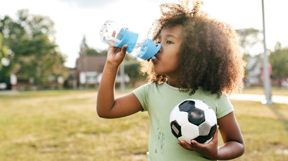 Young girl holding a soccer ball and drinking water at a sports camp