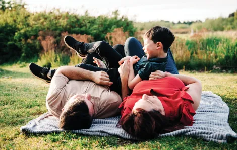 Parents laying on blanket in grass holding up laughing child