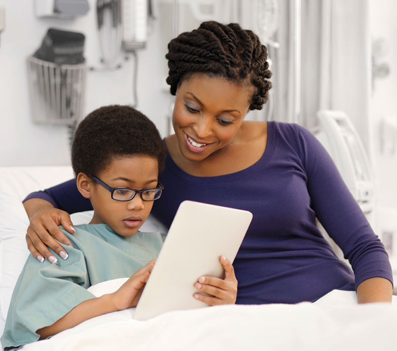 mother and son on hospital bed looking at tablet