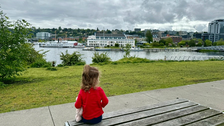 Young girl sitting a bench looking at Lake Union and Mohai