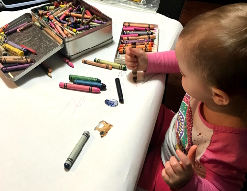 "Toddler drawing with crayons on a giant piece of butcher paper on a table"