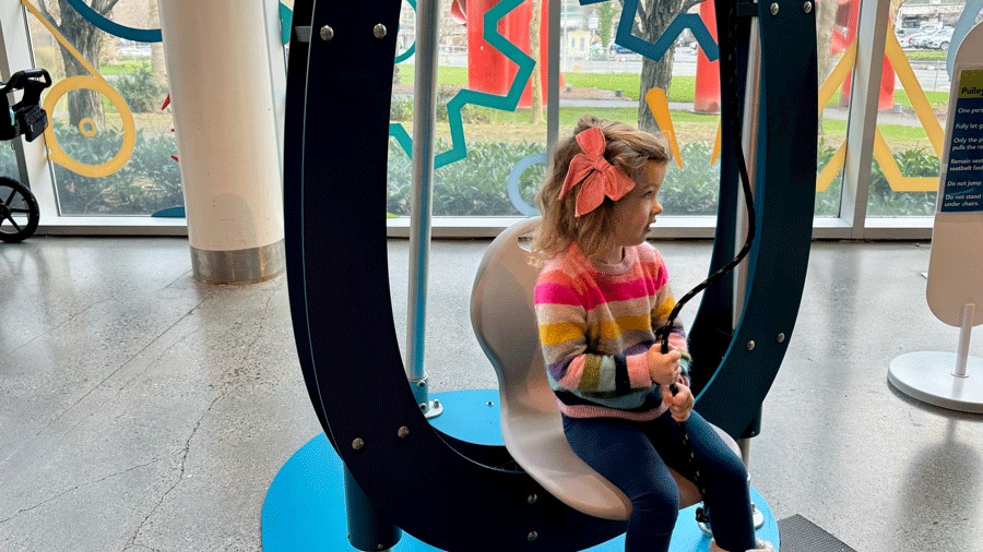 girl pulling herself up with pulleys in the Physics Playground at Pacific Science Center, a family attraction in Seattle