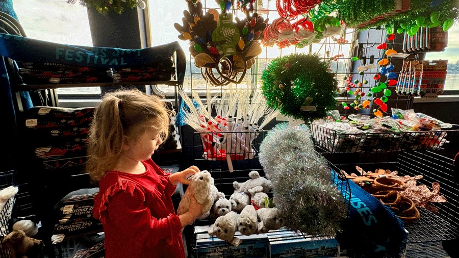 Young girl holding a seal plushie in the Argosy Christmas gift shop onboard the Spirit of Seattle Christmas Ship