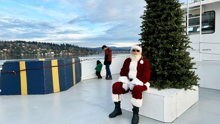 Santa on the outdoor deck of the Argosy Christmas Ship posing for photos in front of the Christmas tree