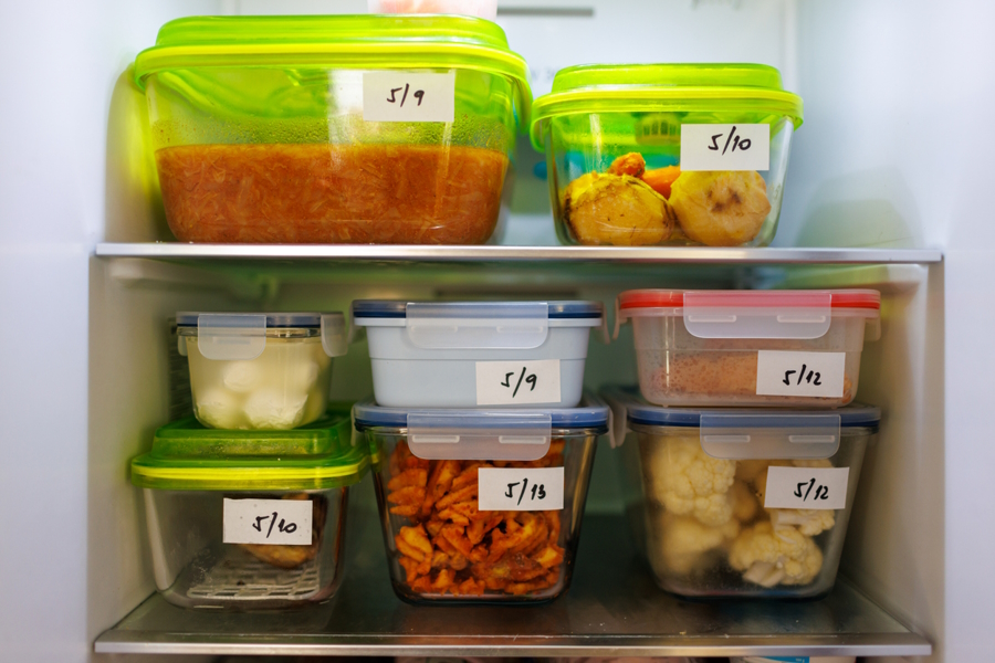 Clear glass containers in a fridge labled with dates for leftover foods.