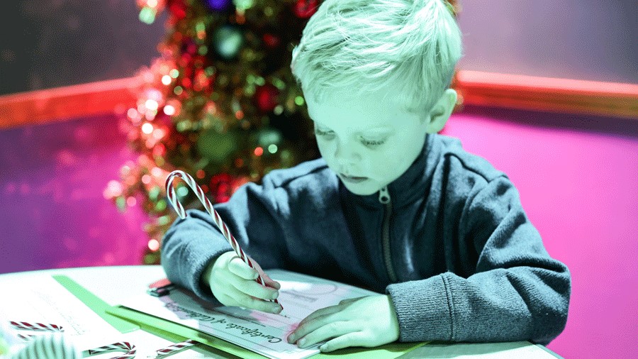 boy writing certificate of authenticity in Santa's Workshop at Kringle's Inventionasium, a Seattle holiday experience for families