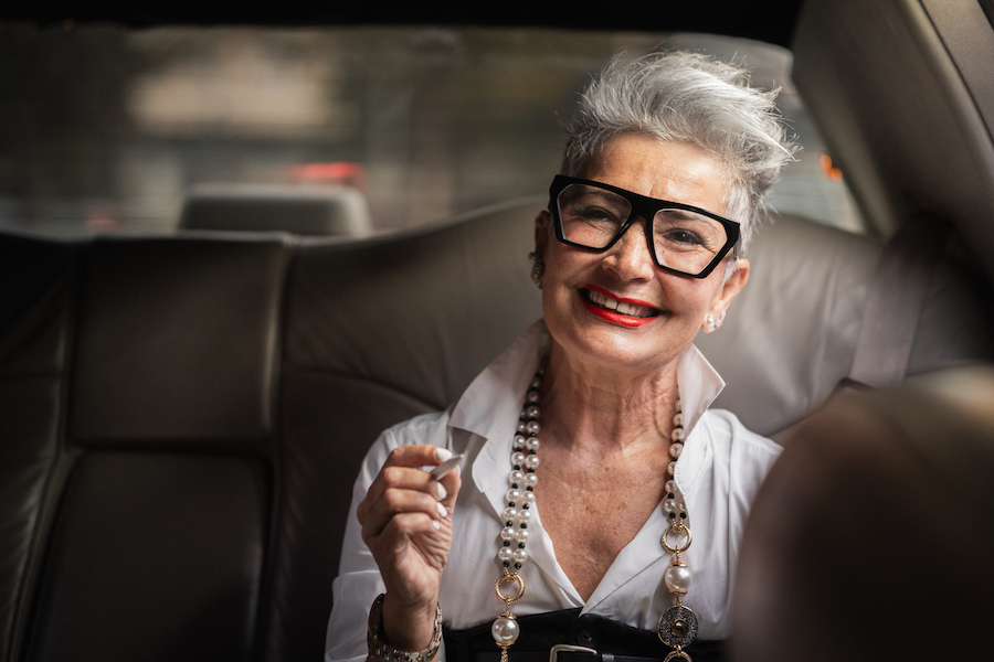 woman with grey hair in a car wearing red lipstick and big glasses