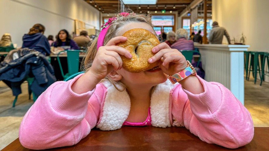 a young girl enjoys a bagel at Oxbow Bagels, one of the top bagel shops in Seattle for families