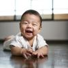 Cute baby on the floor smiling five factors for baby to thrive