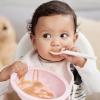 Baby in a highchair holding an empty bowl and spoon as a signal for baby led weaning