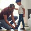 dad tying son shoe kneeling down helping child