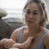 an overwhelmed mom looks into the camera while holding her baby