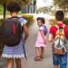 Three kids walking down the sidewalk to school together