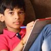 young boy writing in a note pad by himself looks at the camera with a serious expression