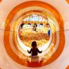 Young girl at an indoor playground slides down the colorful slide into the ball pit at Twinkle Land Play Cafe 