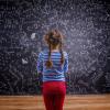 child standing looking at a blackboard covered with math