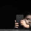 a young child from the anxious generation with a cell phone in hand against a dark background