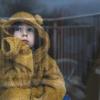 child in a bear hoodie looking out a window experiencing winter burnout