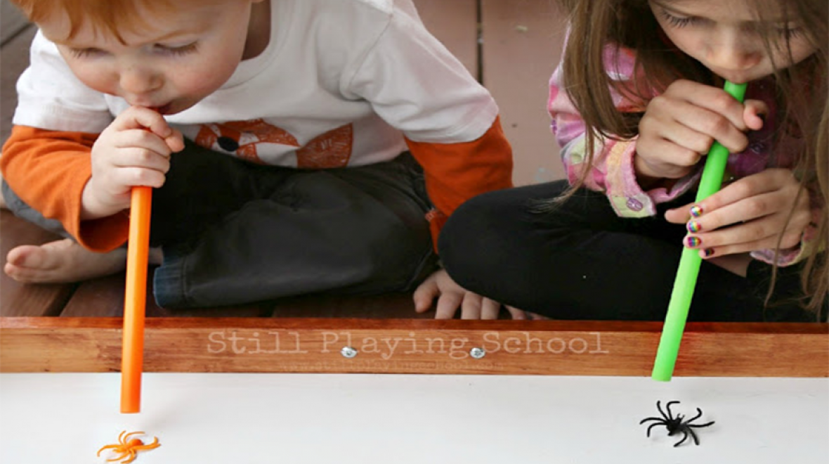 two kids blow plastic spiders with straws while playing a Halloween party game for kids