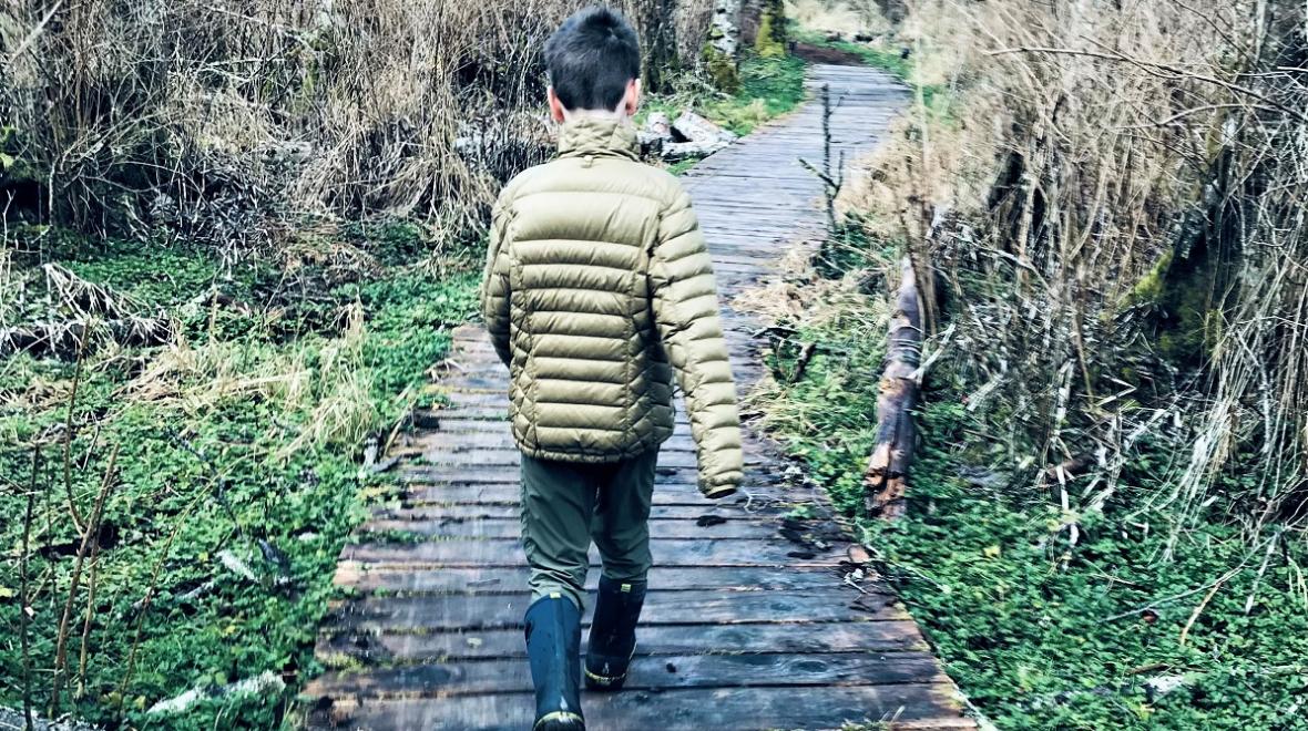 Boy in a green coat hiking along a boardwalk on Whidbey Island, hiking native forest land is among Whidbey's best activities with kids