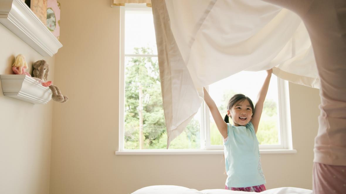 mother and daughter lifting a new bedding sheet onto a bed