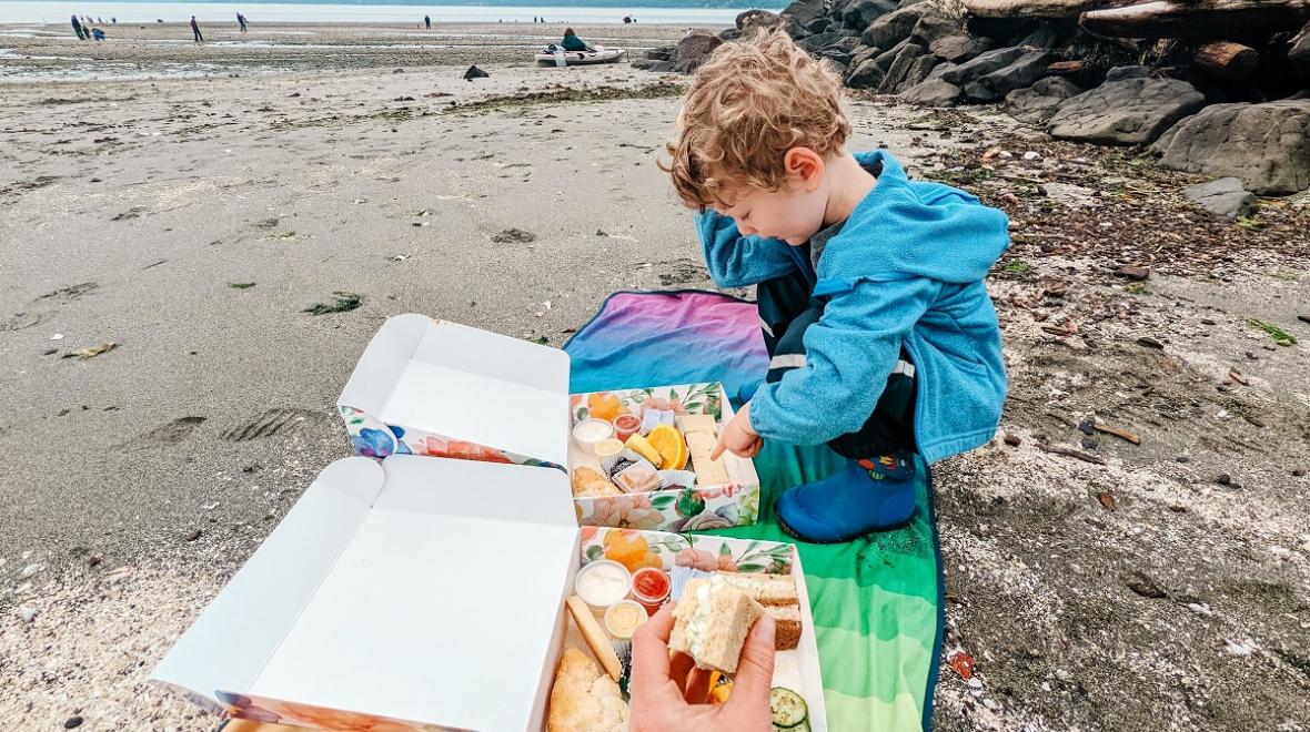 Boy standing on the beach with a box of treats from the Secret Garden Tea Room