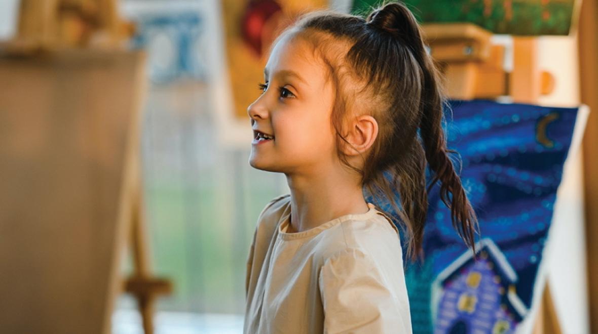 Young girl looking excited standing in front of painting canvas 