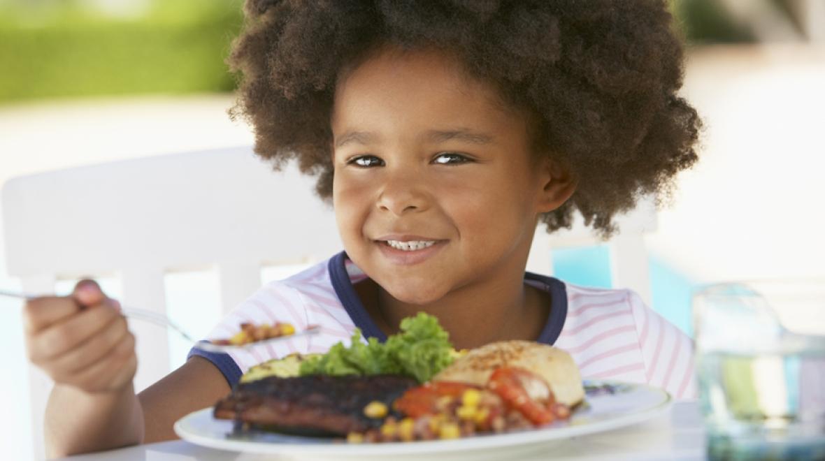 Young kid eating a plate of food at a BBQ