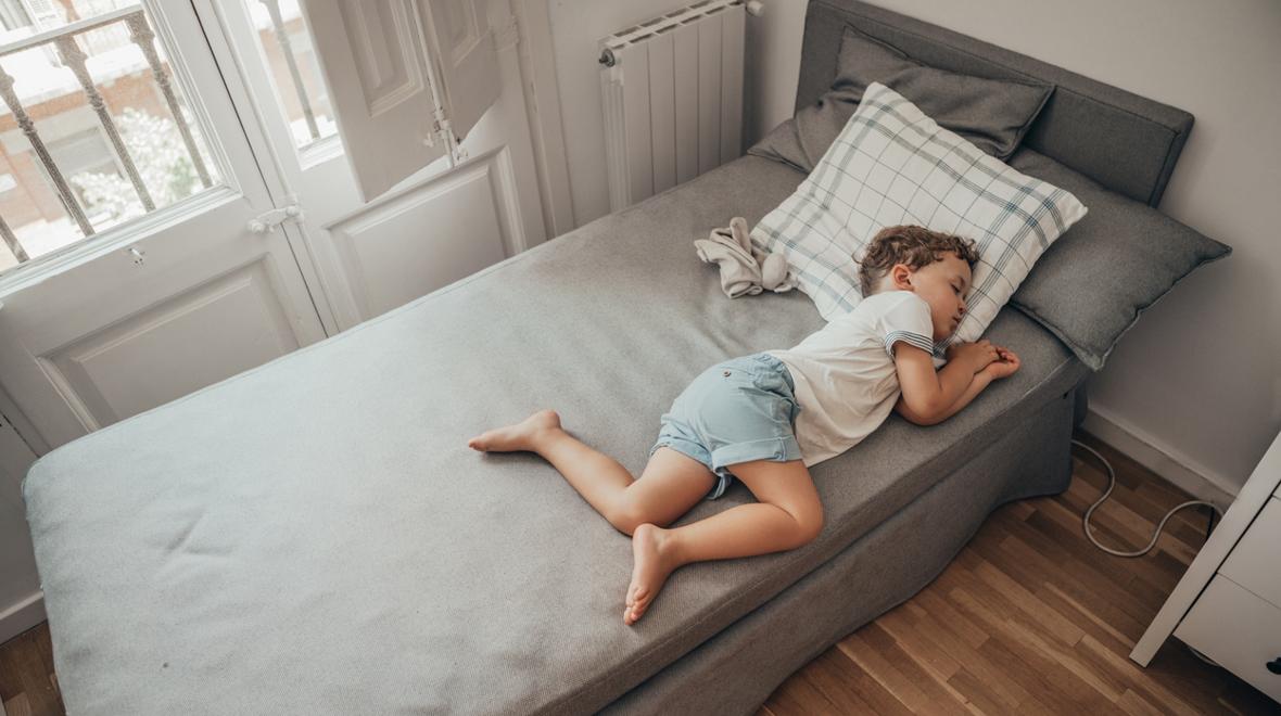 Boy sleeping in a bed when it is hot in the summer