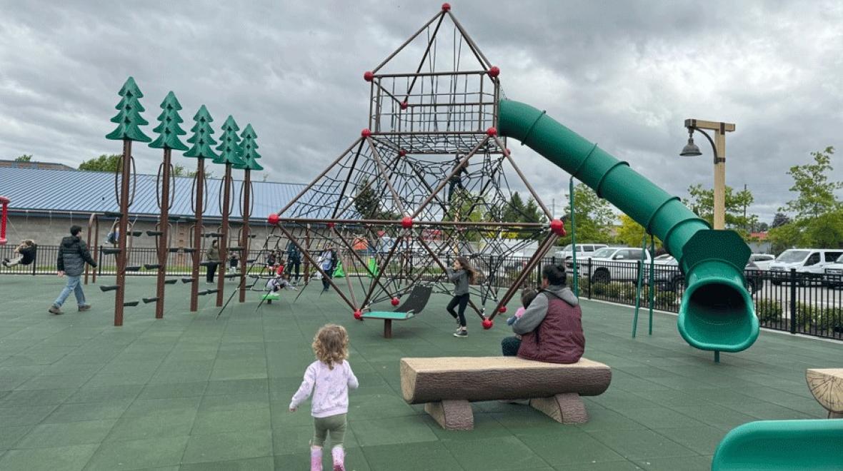 Young girl runs toward a new inclusive playground in Snohomish, near Seattle, with large climbing structures