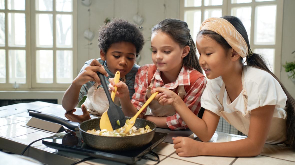 Three kids wearing aprons and cooking together and enjoying indoor summer activities at home