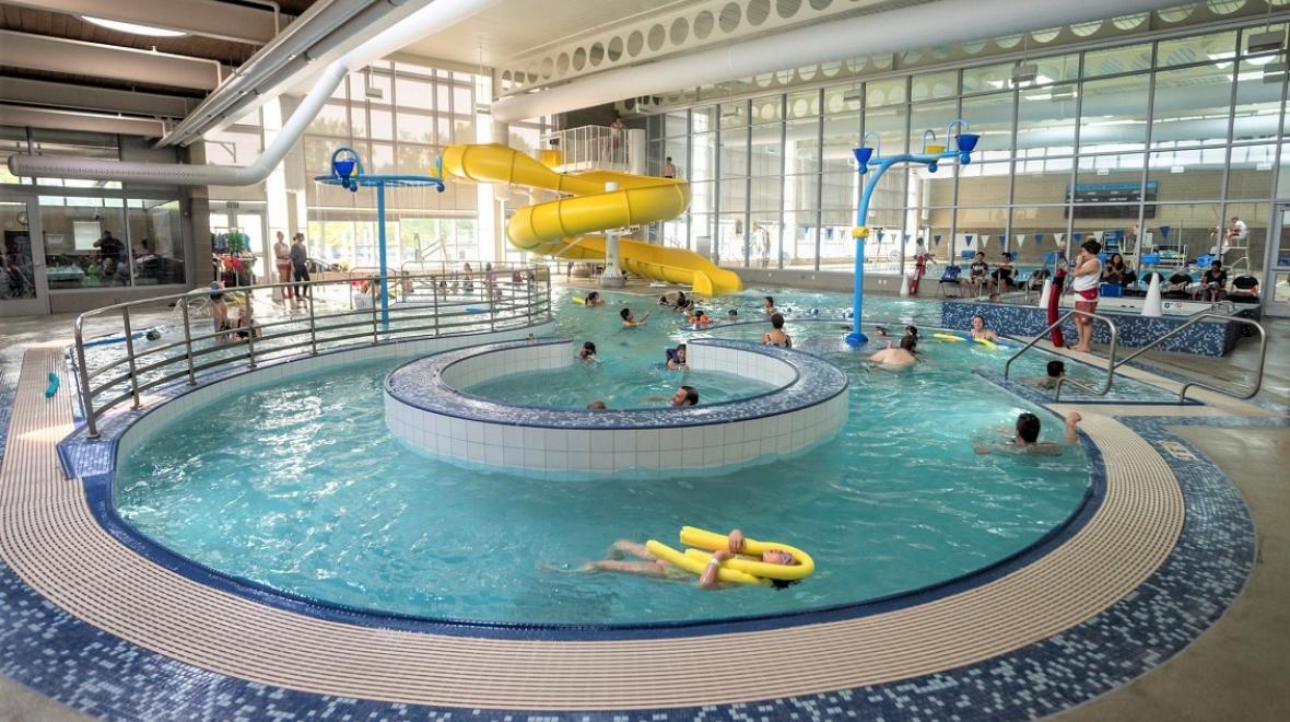 View of people swimming in Rainier Beach indoor Pool in Seattle. Yellow twister slide is in the background and the lazy river feature is in the foreground