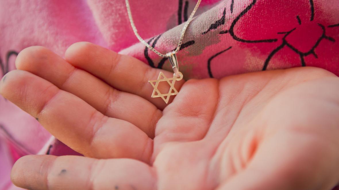A Jewish child's hand holds a necklace with a Star of David charm