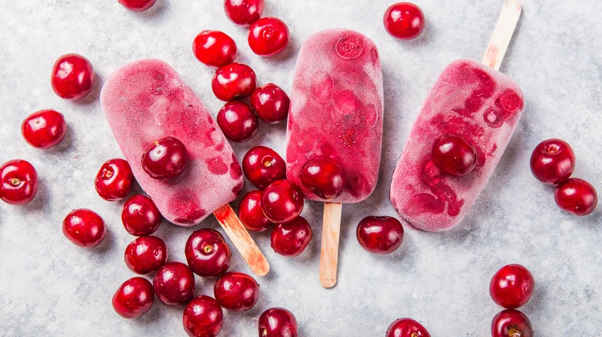 Cherry popsicles lying on a table with cherries all around them are a great summertime treat