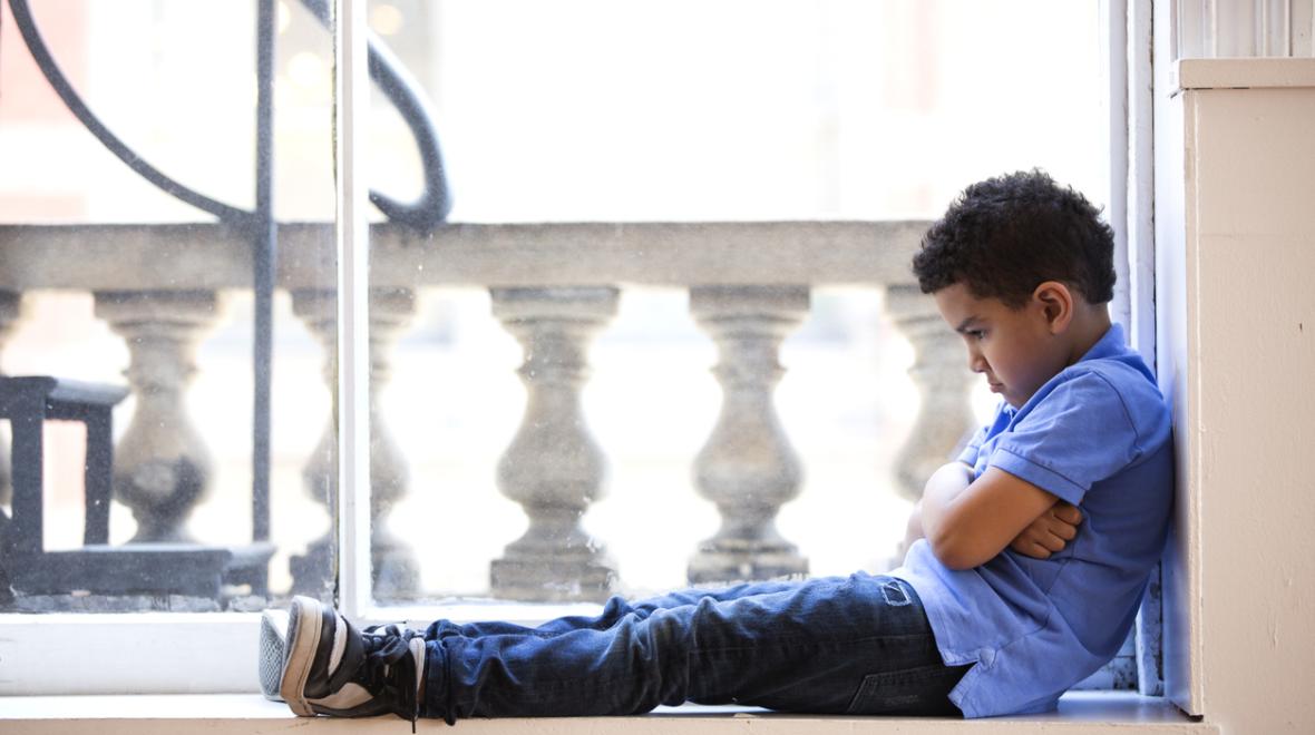 a child sits in a window looking defeated and helpless