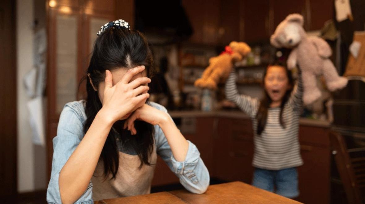 a mom covering her eyes, contemplating her gentle parenting techniques, while child throws a tantrum