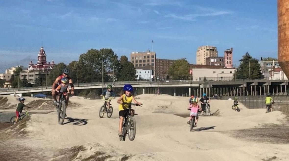 Kids and a dad with a baby on his bike ride on the pump track at Bellingham's Waypoint Park outside of Seattle