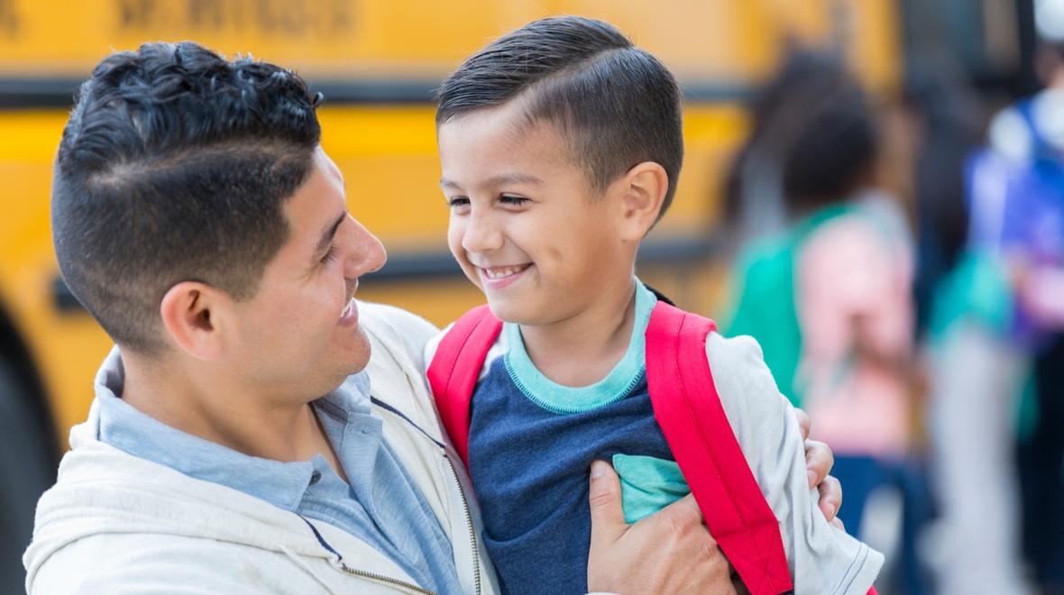 Boy with a red backpack smiling with is father because he's overcome school anxiety