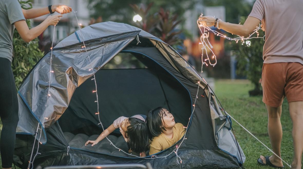 Family setting up a tent and a string of lights for backyard camping