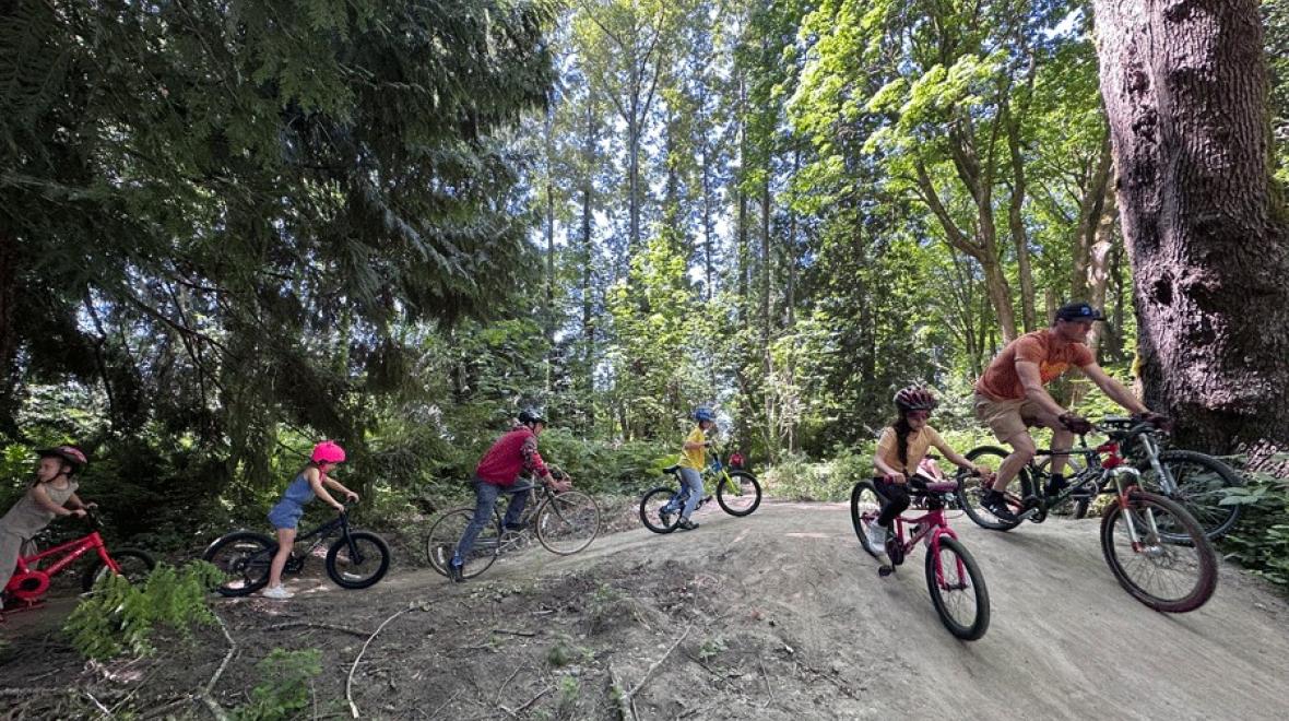 Families ride bikes through the Cedar Lanes Park pump track, a Seattle-area bike pump track