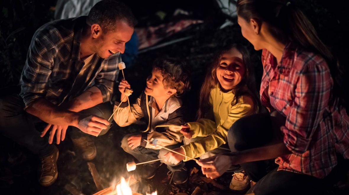 Families around a campfire roasting marshmallows and playing a campfire game