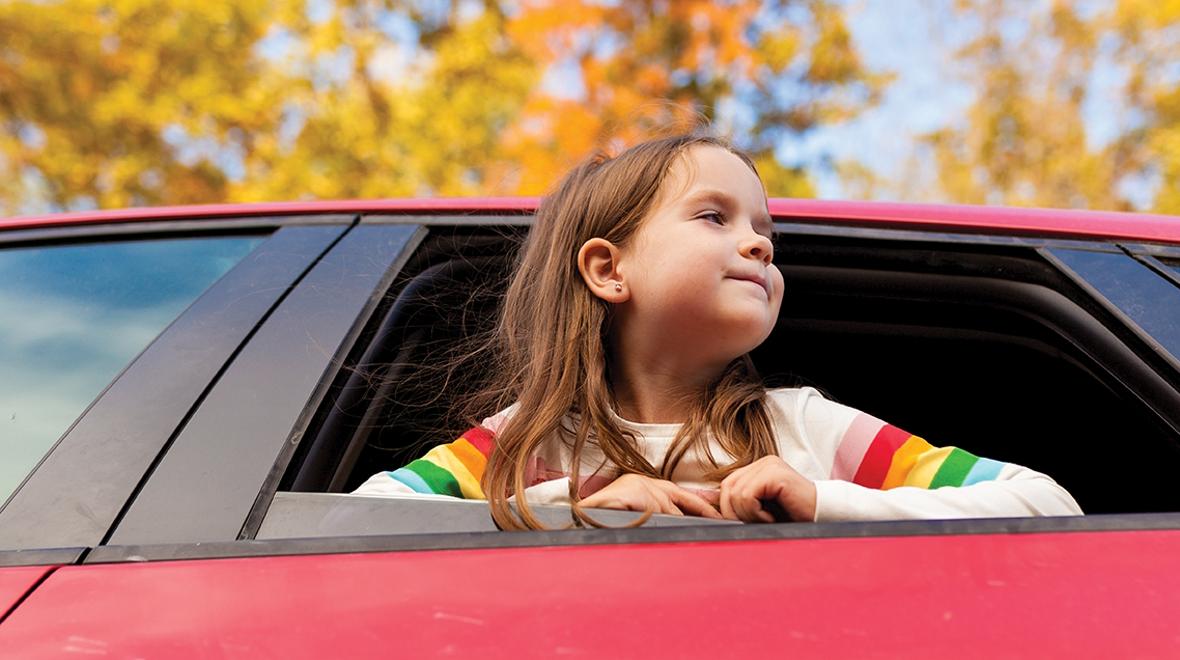 Girl with her head out the window of a car looking at fall leaves on a scenic drive in the Pacific Northwest