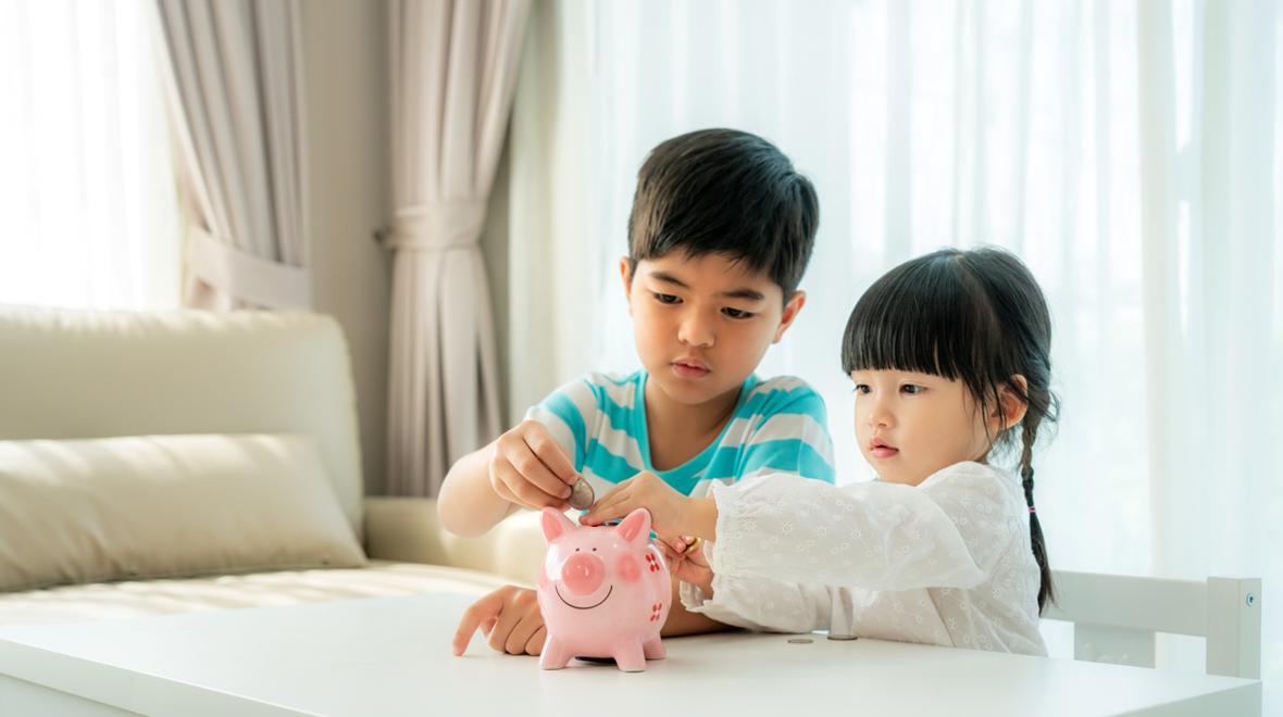 Kids learning to save money putting coins in a piggy bank