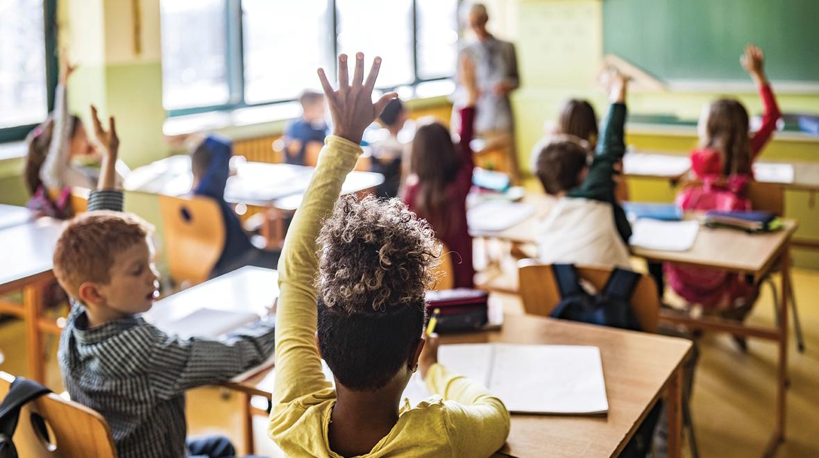 Classroom at school full of students, several raising their hands to answer a question