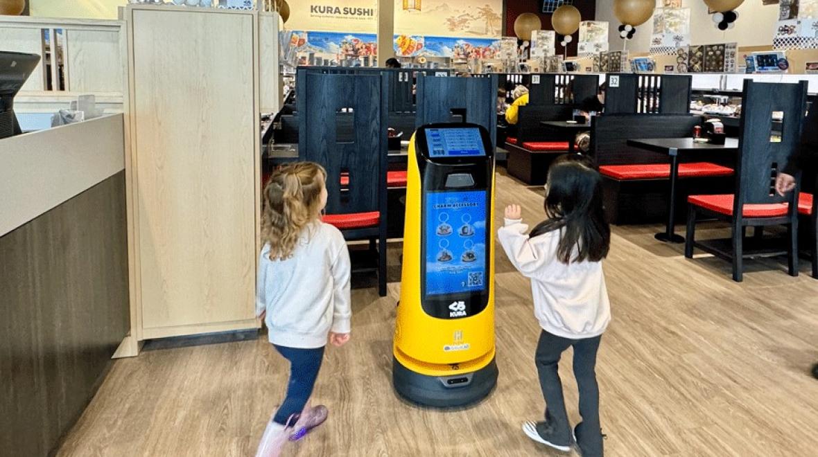 A robot greets two kids at Kura Sushi, a Seattle-area robot restaurant with a sushi conveyor belt