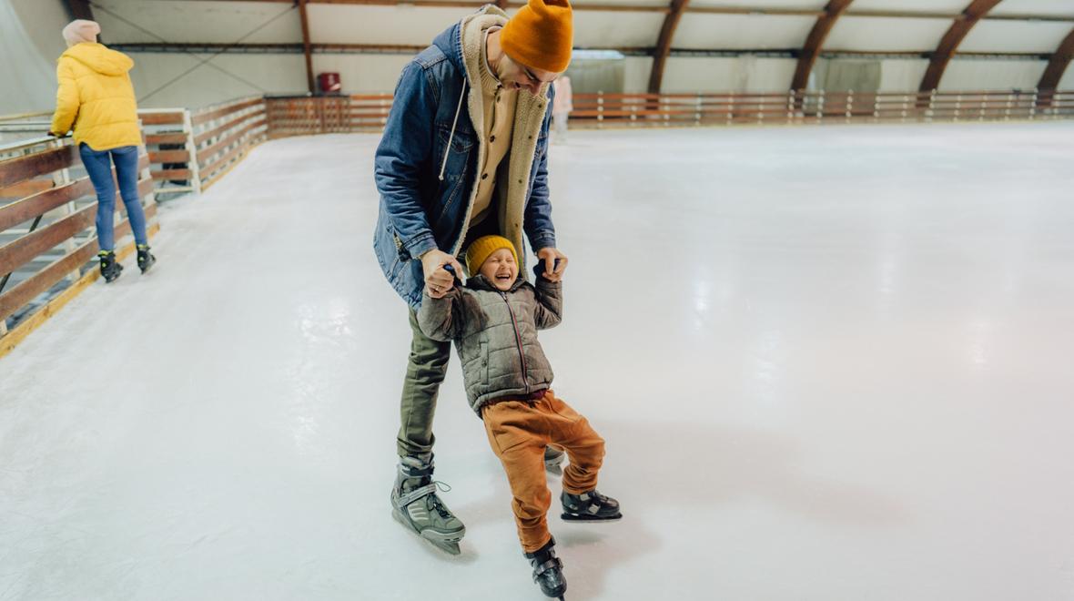 Boy and his dad learning to ice skate at an outdoor holiday ice-skating rink near Seattle